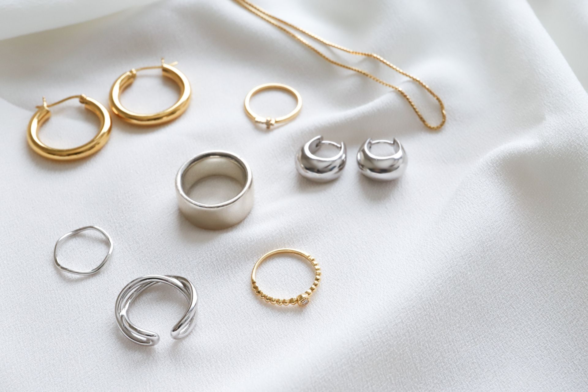 An assortment of gold and silver rings, earrings, and a necklace laid on white fabric.