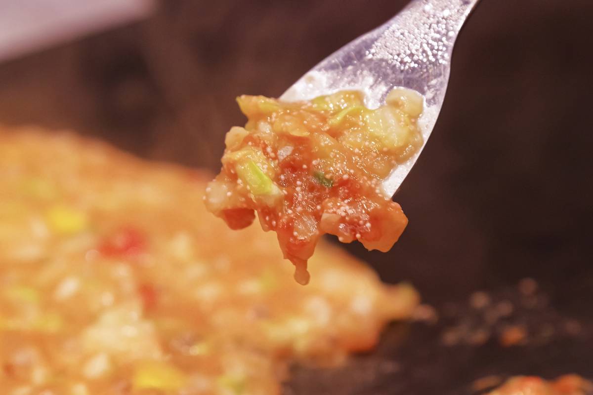 A clear plastic fork lifts a spoonful of steaming, chunky food from a hot griddle.