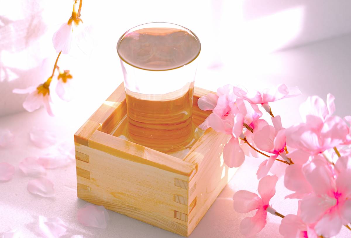A glass of liquid in a wooden masu, surrounded by pink cherry blossoms.