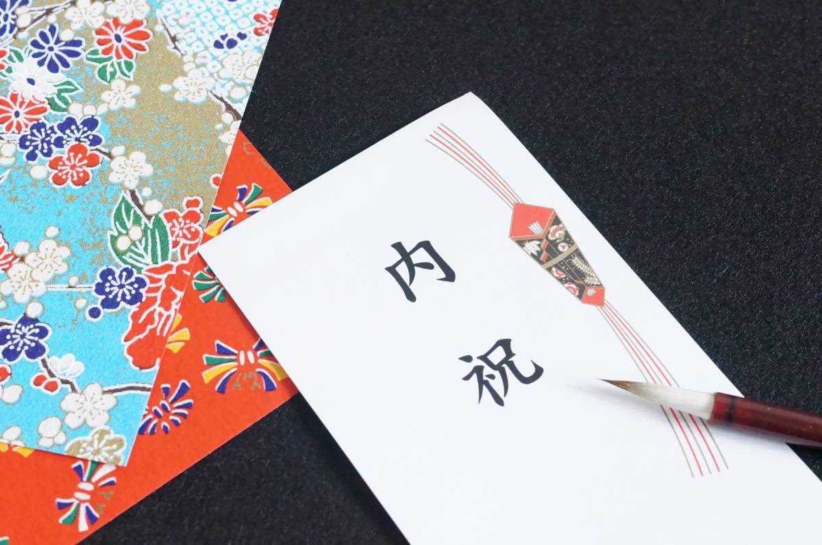 A white envelope with Japanese characters and a decorative red knot, a calligraphy brush