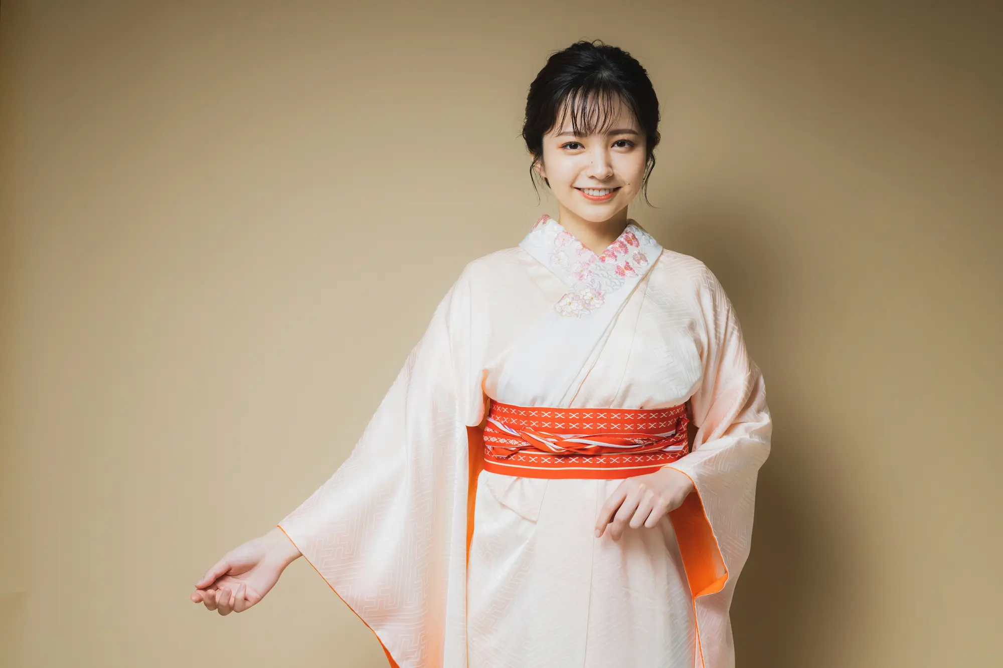 A smiling young woman in a light pink kimono with a red obi.
