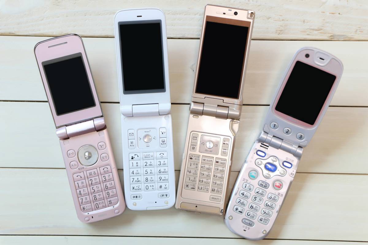 Four open pastel-colored flip phones on a light wooden surface.