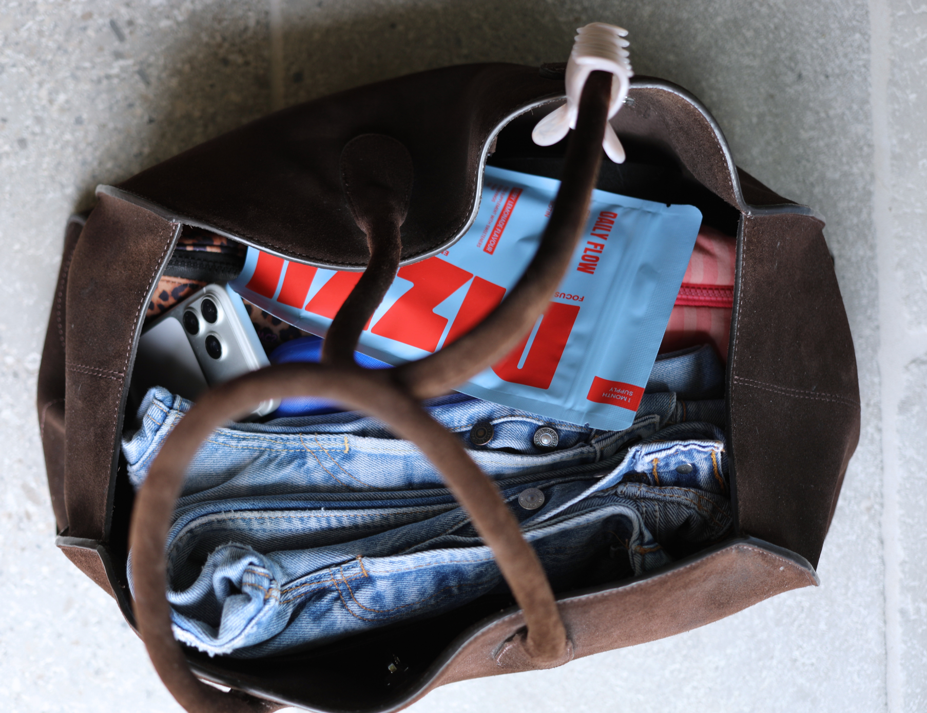An open weekend bag packed with denim and a blue Daily Flow pouch