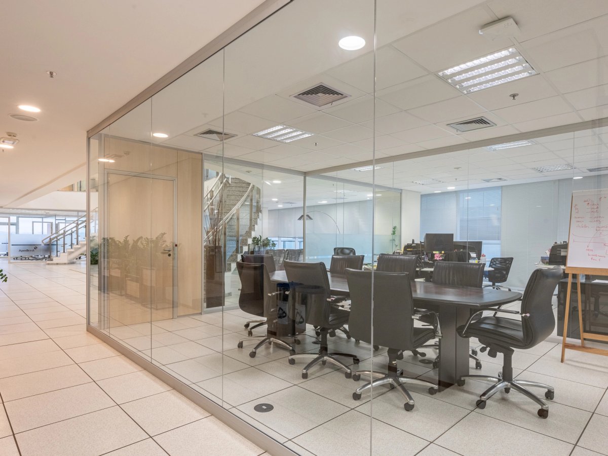 Sala de reunião envidraçada em um andar corporativo amplo, linha Ackua.