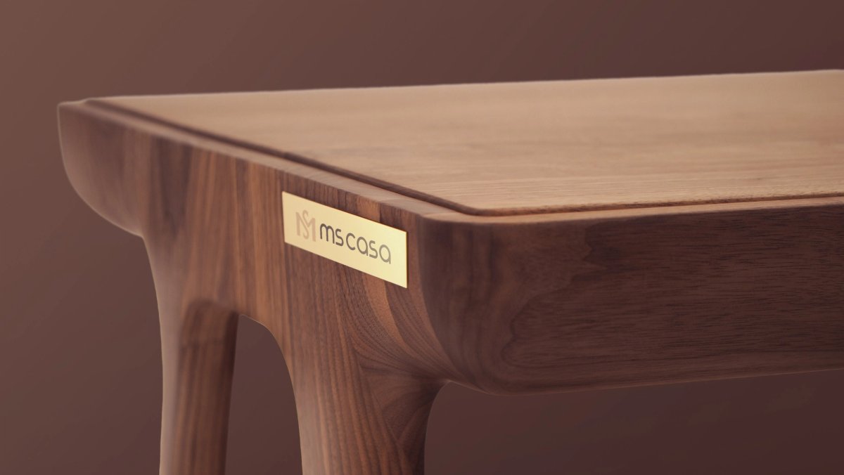 Plaqueta dourada com a marca aplicada em uma mesa de madeira.
