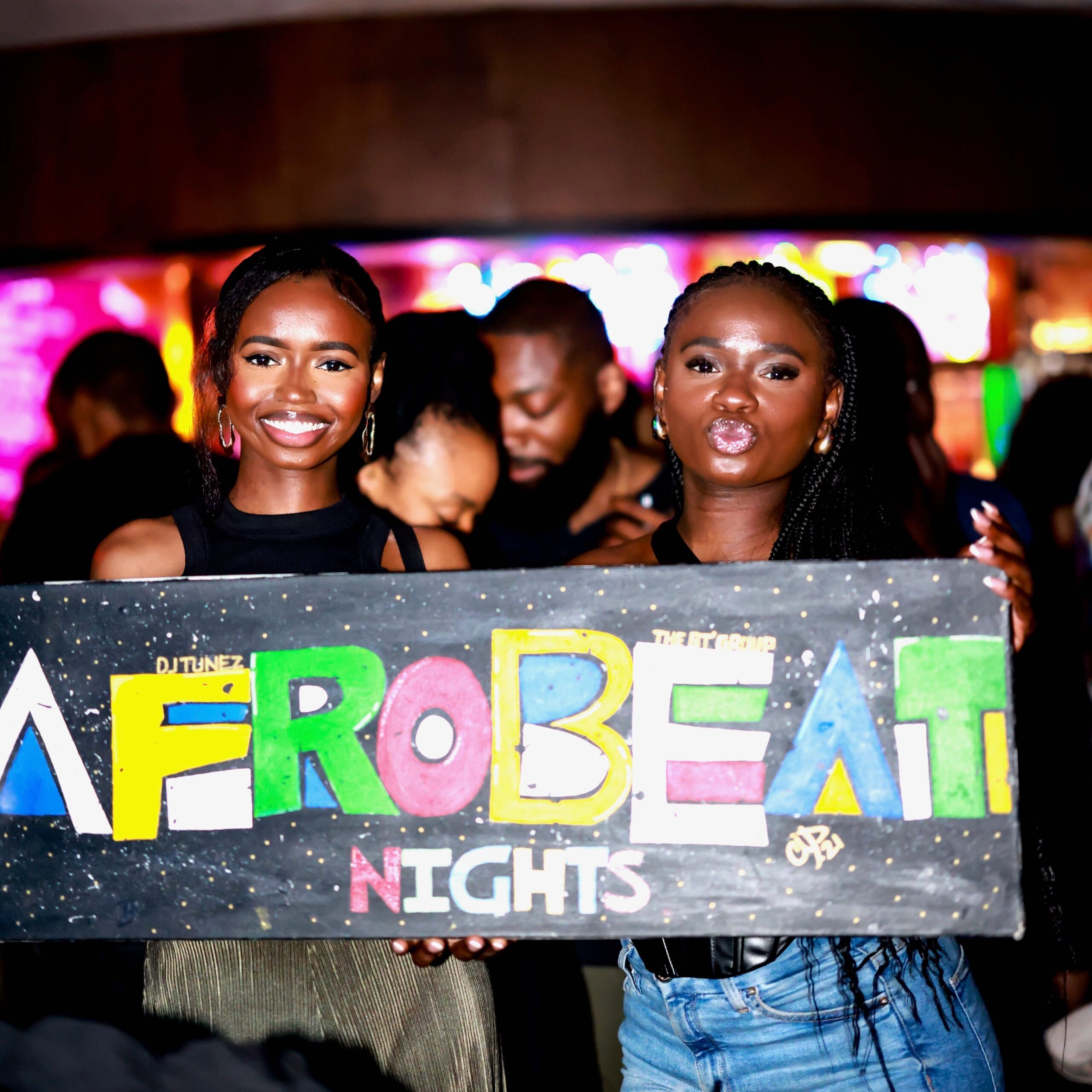 Two guests holding the hand-painted Afrobeat Nights sign