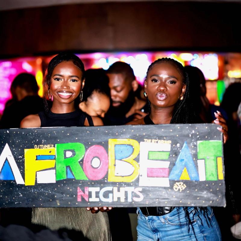 Two guests holding the hand-painted Afrobeat Nights sign