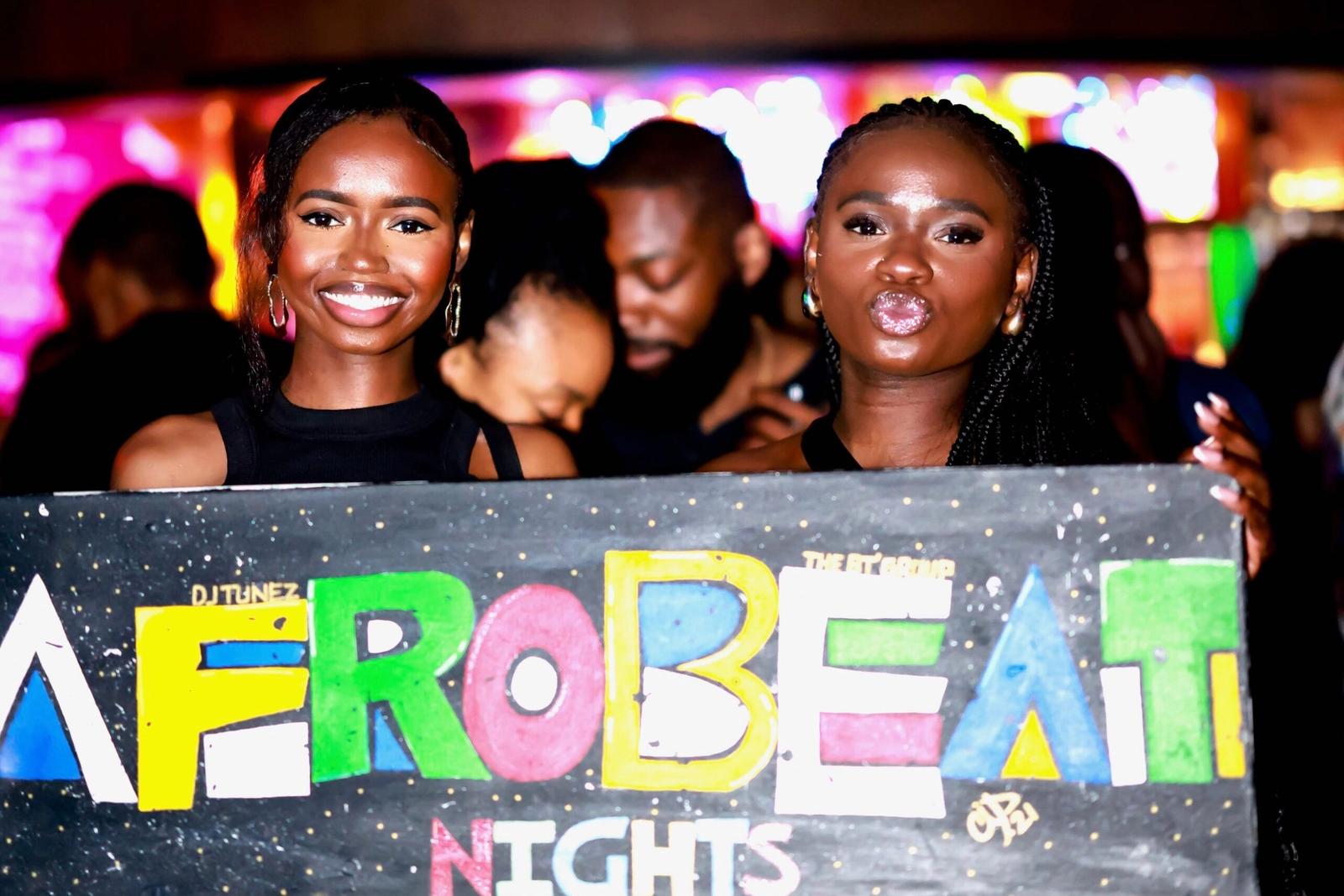 Two guests holding the hand-painted Afrobeat Nights sign