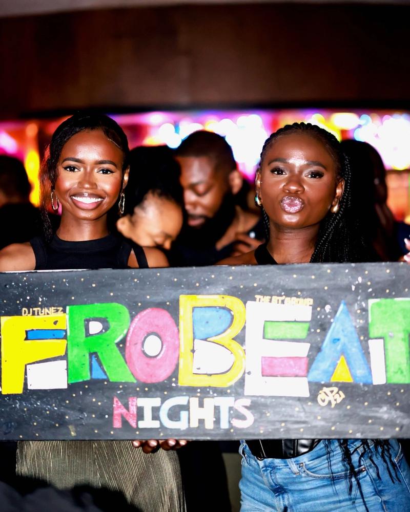 Two guests holding the hand-painted Afrobeat Nights sign