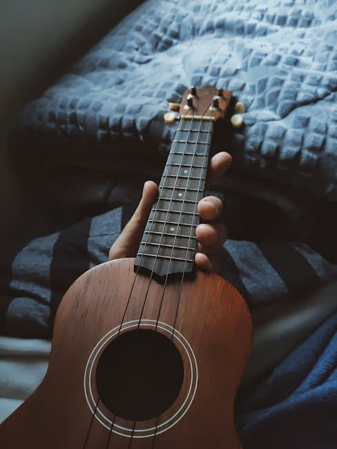 A hand holding a ukulele, showcasing its body and strings, perfect for an article about ukuleles.