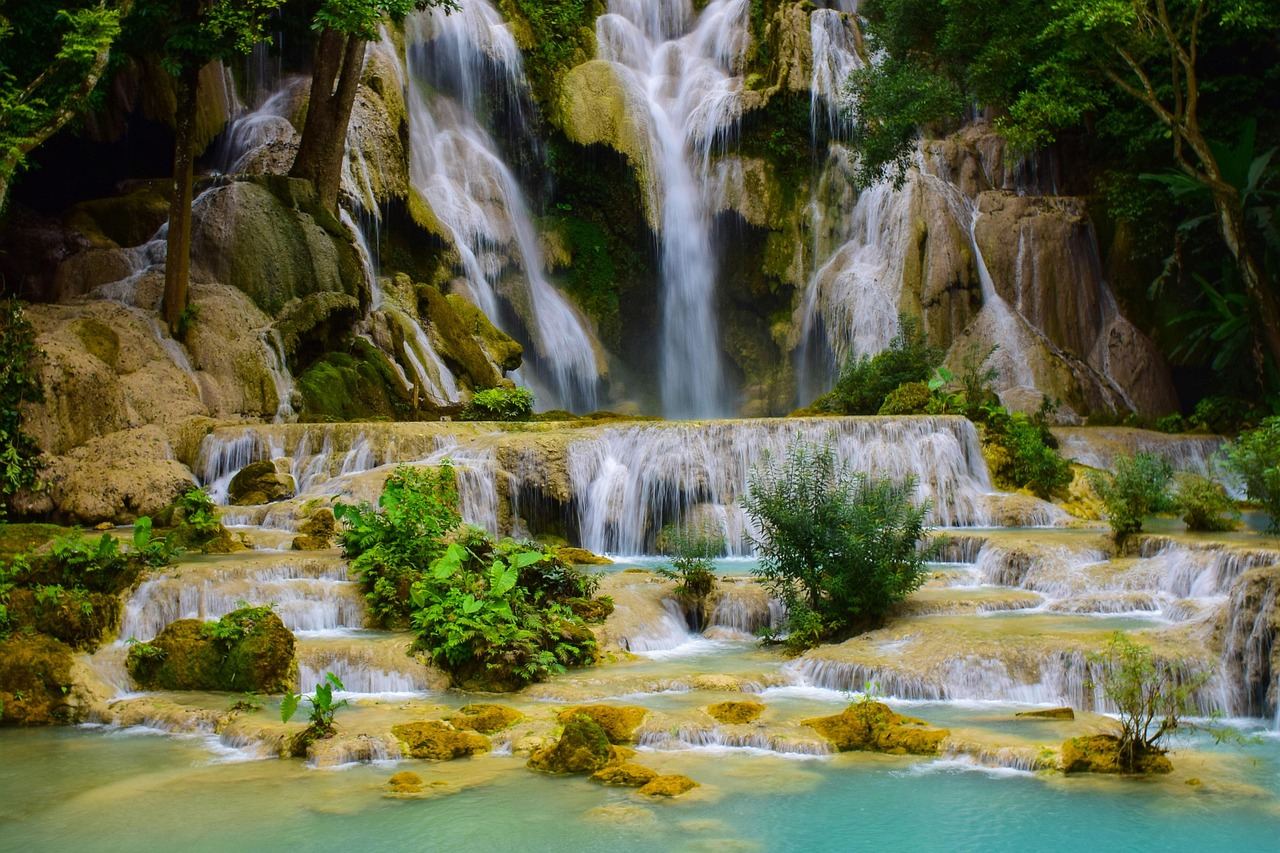 A majestic waterfall cascades down rocky cliffs, surrounded by lush greenery and mist rising from the flowing water.