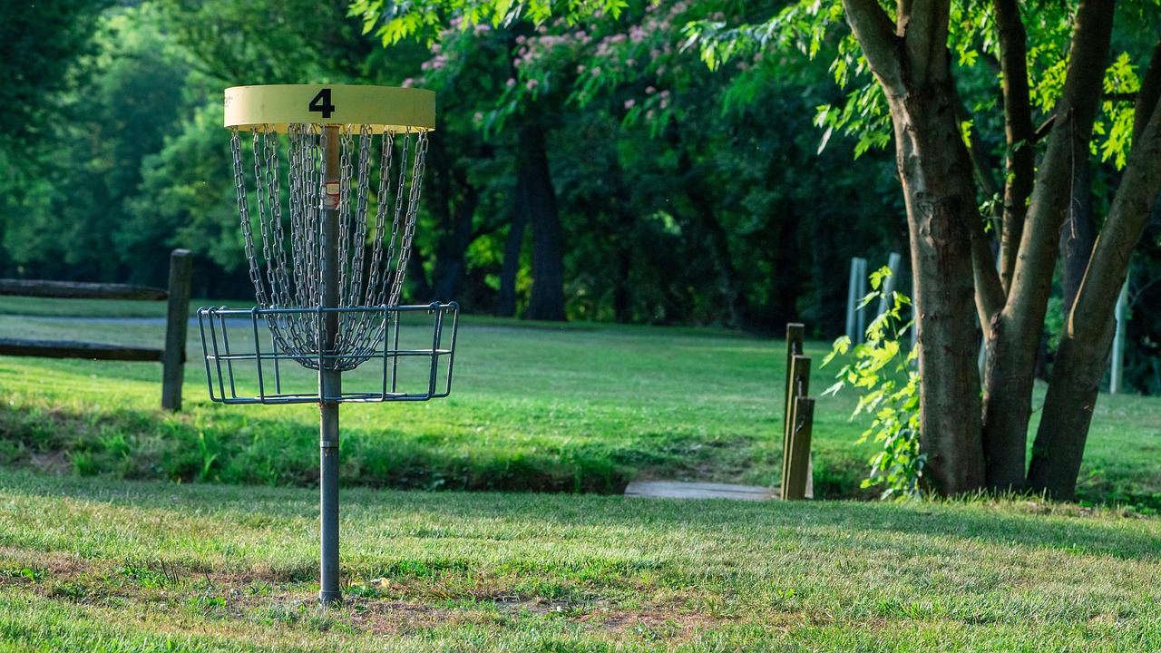 A vibrant disc golf course featuring lush green fairways, colorful baskets, and players throwing discs under a clear blue sky.