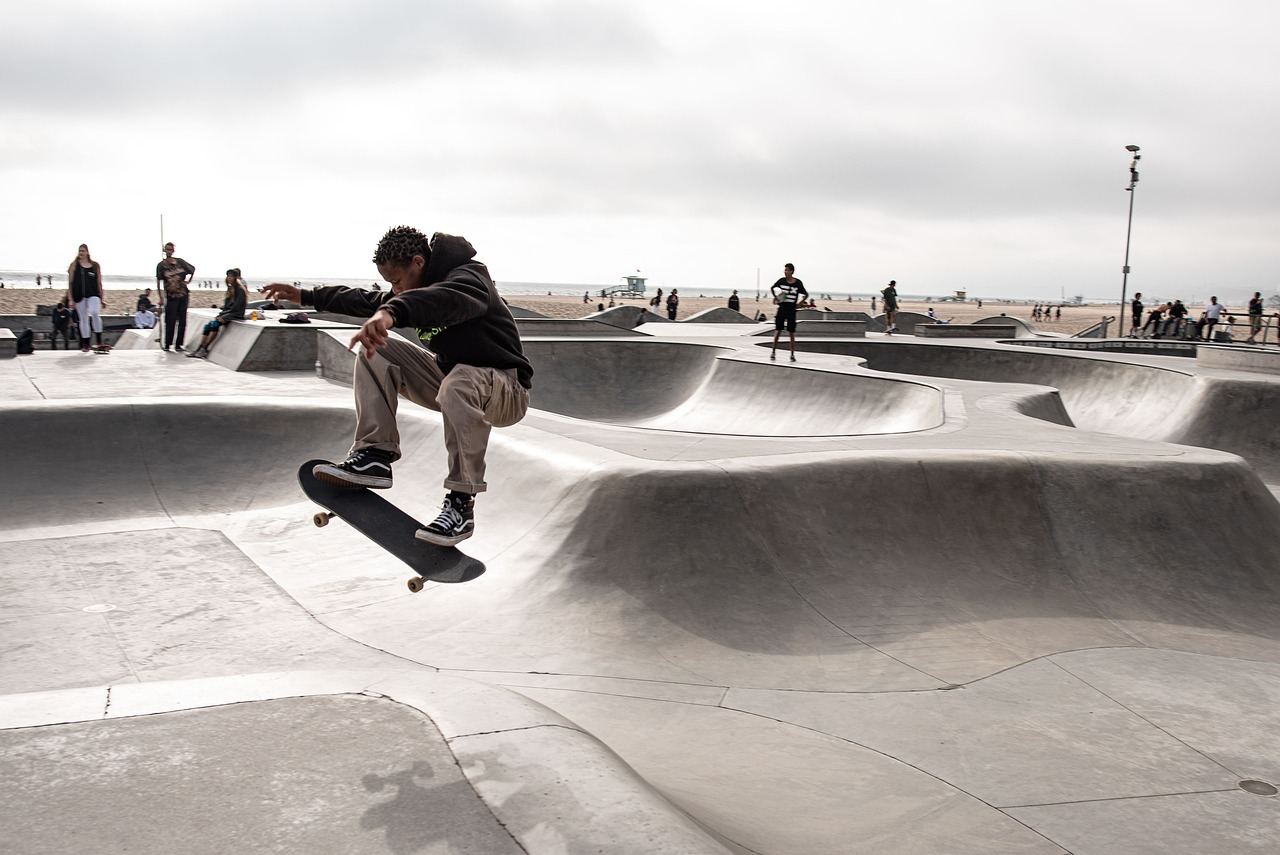 A skateboarder performs a trick mid-air above a vibrant skate park, showcasing skill and excitement.