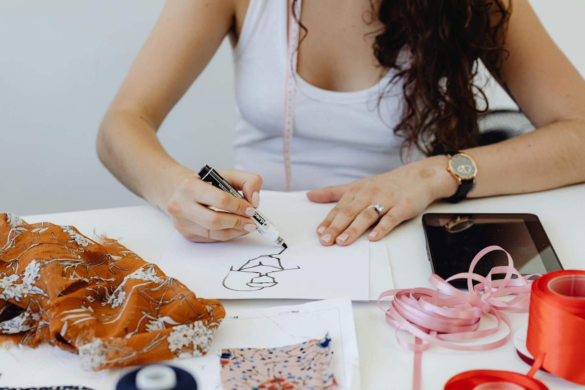 Fashion designer sketching ideas with fabric samples and tools on her table.
