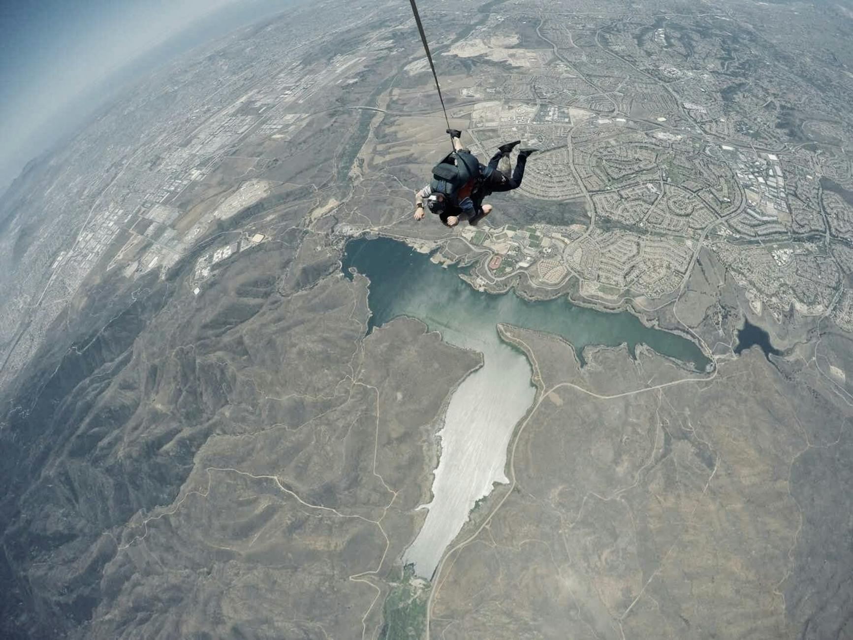 A tandem skydiver experiences the thrill of freefall while surrounded by breathtaking aerial views of the landscape below.