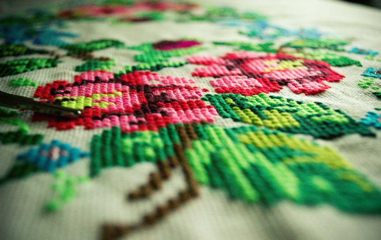 A colorful array of cross-stitched patterns displayed on a wooden table, showcasing intricate designs and vibrant threads.