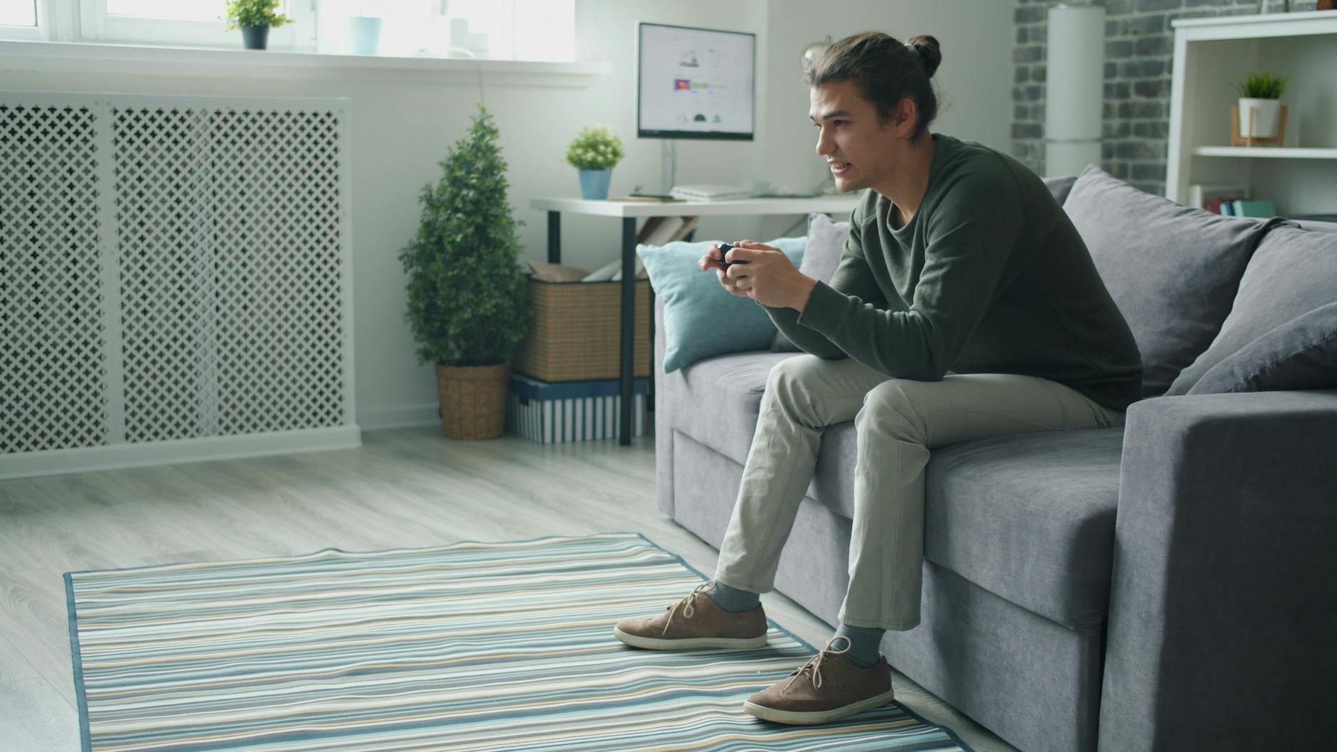 Smiling young man enjoying video games on a sofa at home.