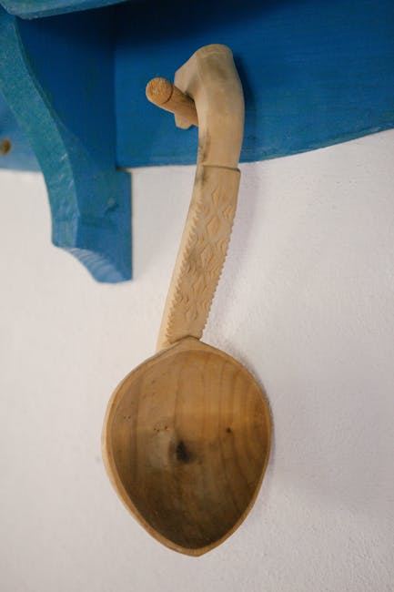 A beautifully carved wooden spoon hanging on a blue shelf, showcasing spoon carving craftsmanship.