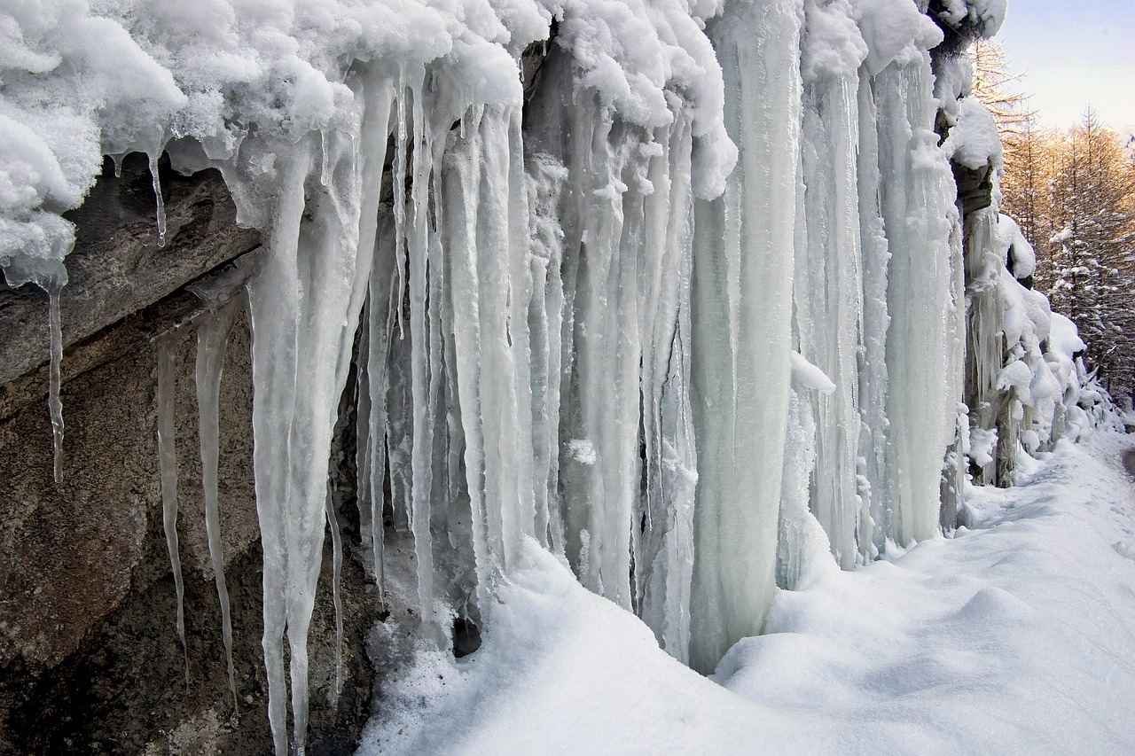 Glittering icicles hang from a rocky cliff, showcasing the icy environment of an ice climbing adventure.