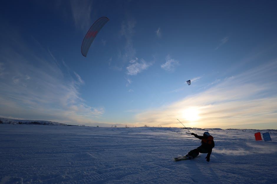 A person snowkiting on a snowy landscape with a colorful kite against a sunset sky.