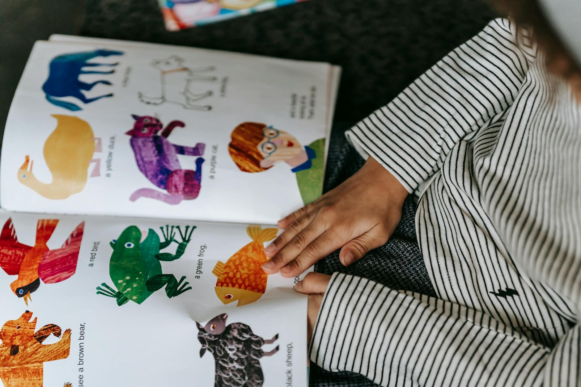 A child's hands hold an open book filled with vibrant illustrations of various animals, capturing their attention.