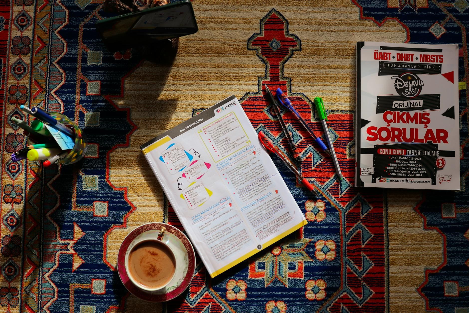 A cozy study setup featuring books, notes, and a steaming cup of coffee on a colorful patterned carpet.