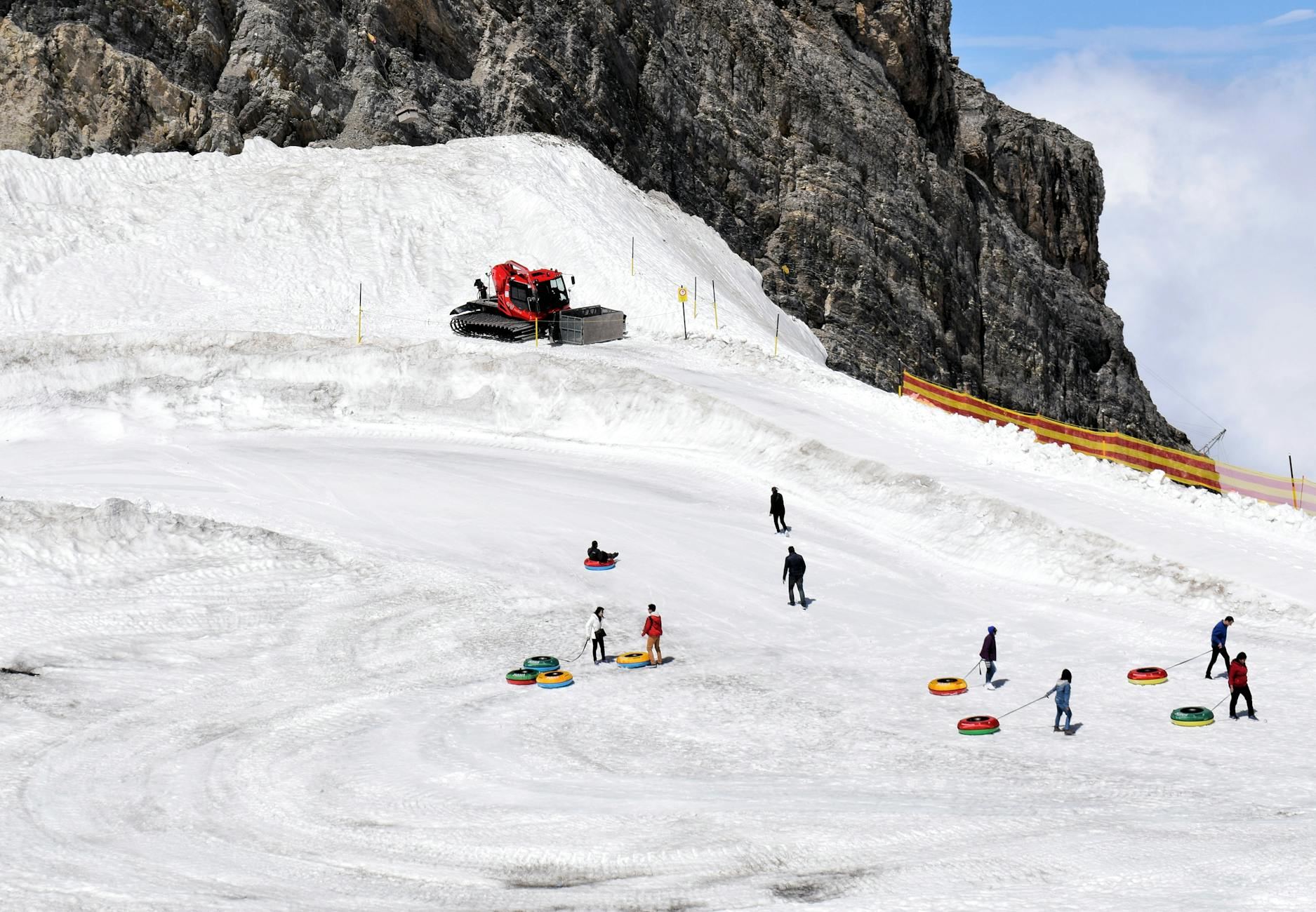 Thrilling snow tubers race down a snowy slope under a bright blue sky at a bustling mountain resort.