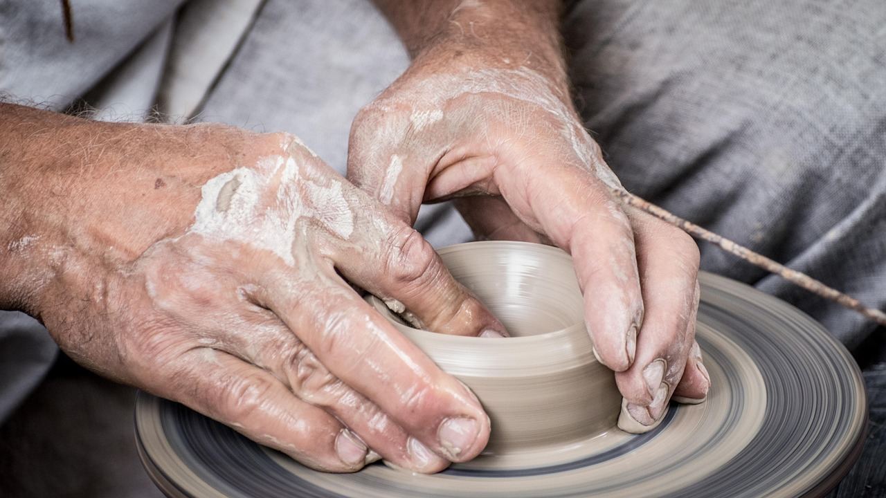A pair of hands skillfully molding a lump of clay into a delicate sculpture on a wooden workbench.