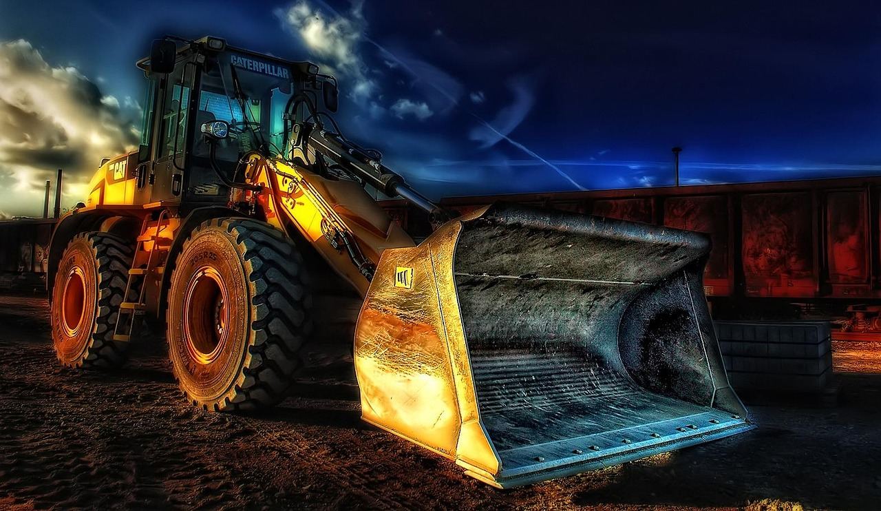 A yellow excavator sits on a grassy field, preparing the site for an outdoor movie screening event.