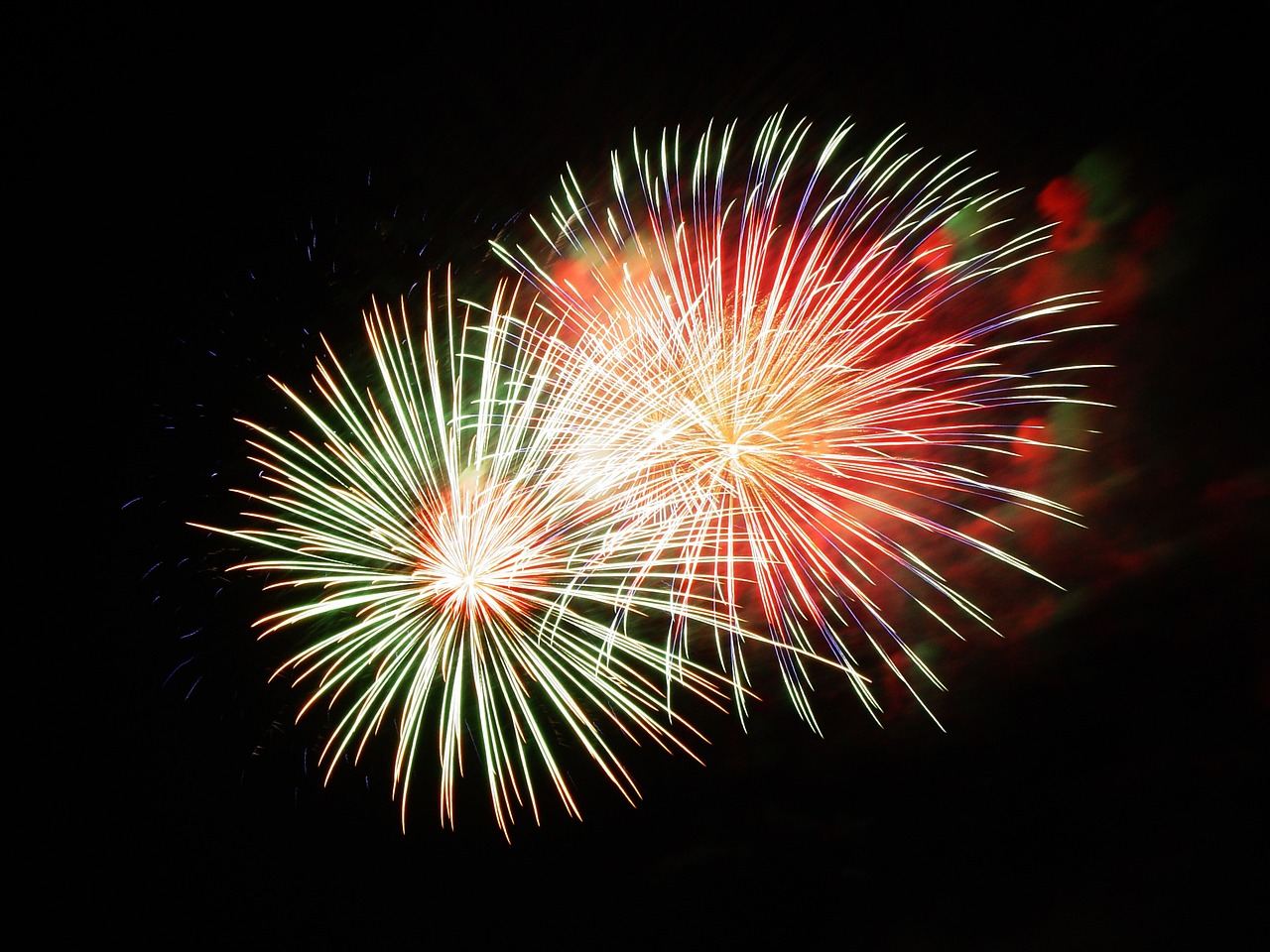 Colorful fireworks burst in the night sky above a dazzling holiday light display, illuminating the festive atmosphere below.