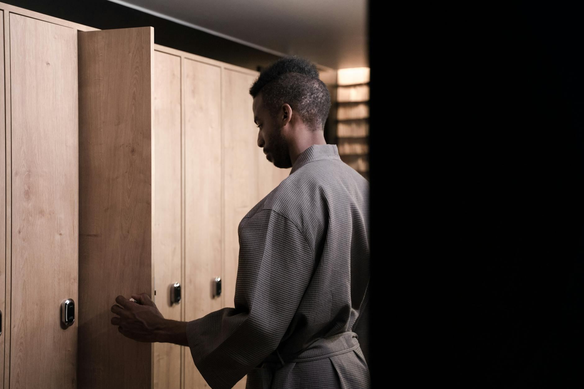 A man in a bathrobe stands by a locker in a tranquil, modern spa environment.