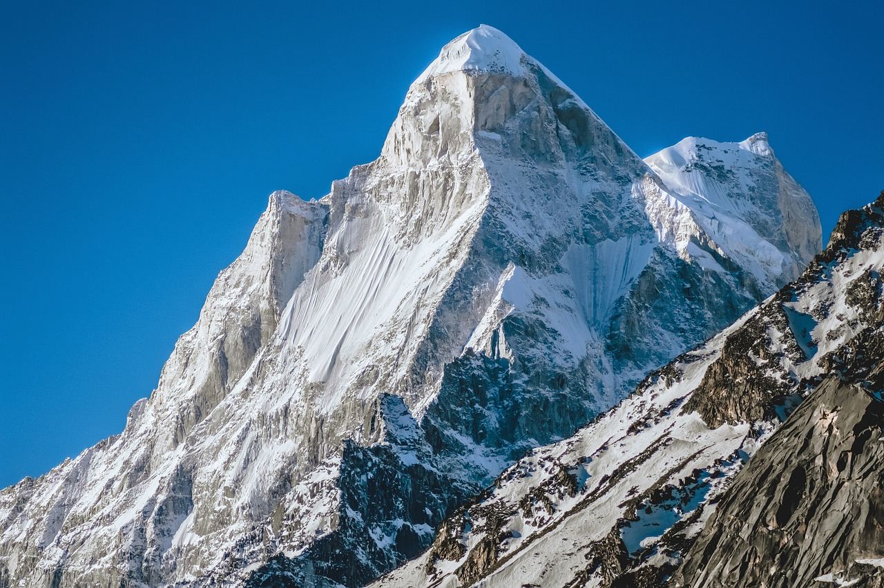 Snow-capped mountains rise majestically under a clear blue sky, inviting adventurers to explore their untouched slopes.
