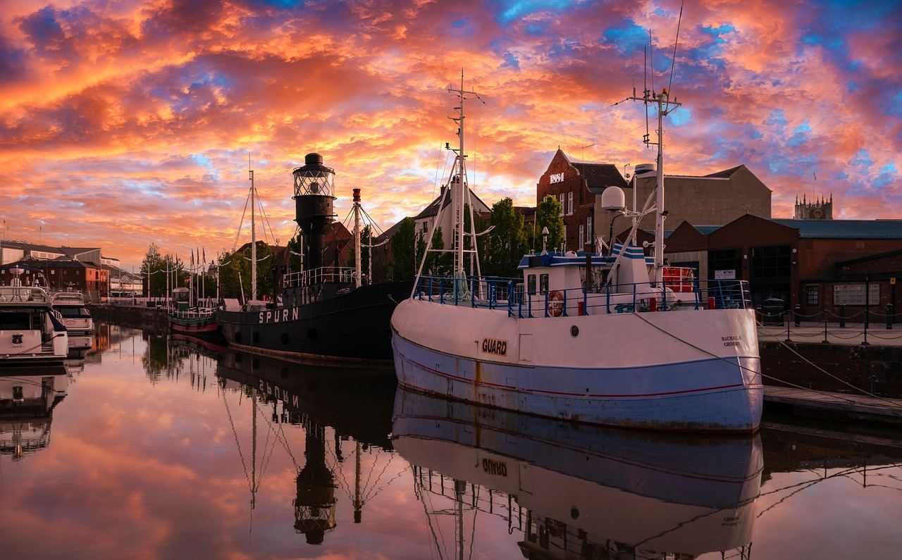 A vibrant sunset casts golden hues over the tranquil waters of Hull Marina, with silhouettes of boats gently bobbing in the foreground.