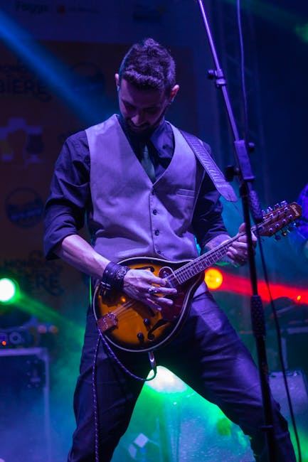 A musician passionately playing a mandolin on stage with vibrant lights in the background.
