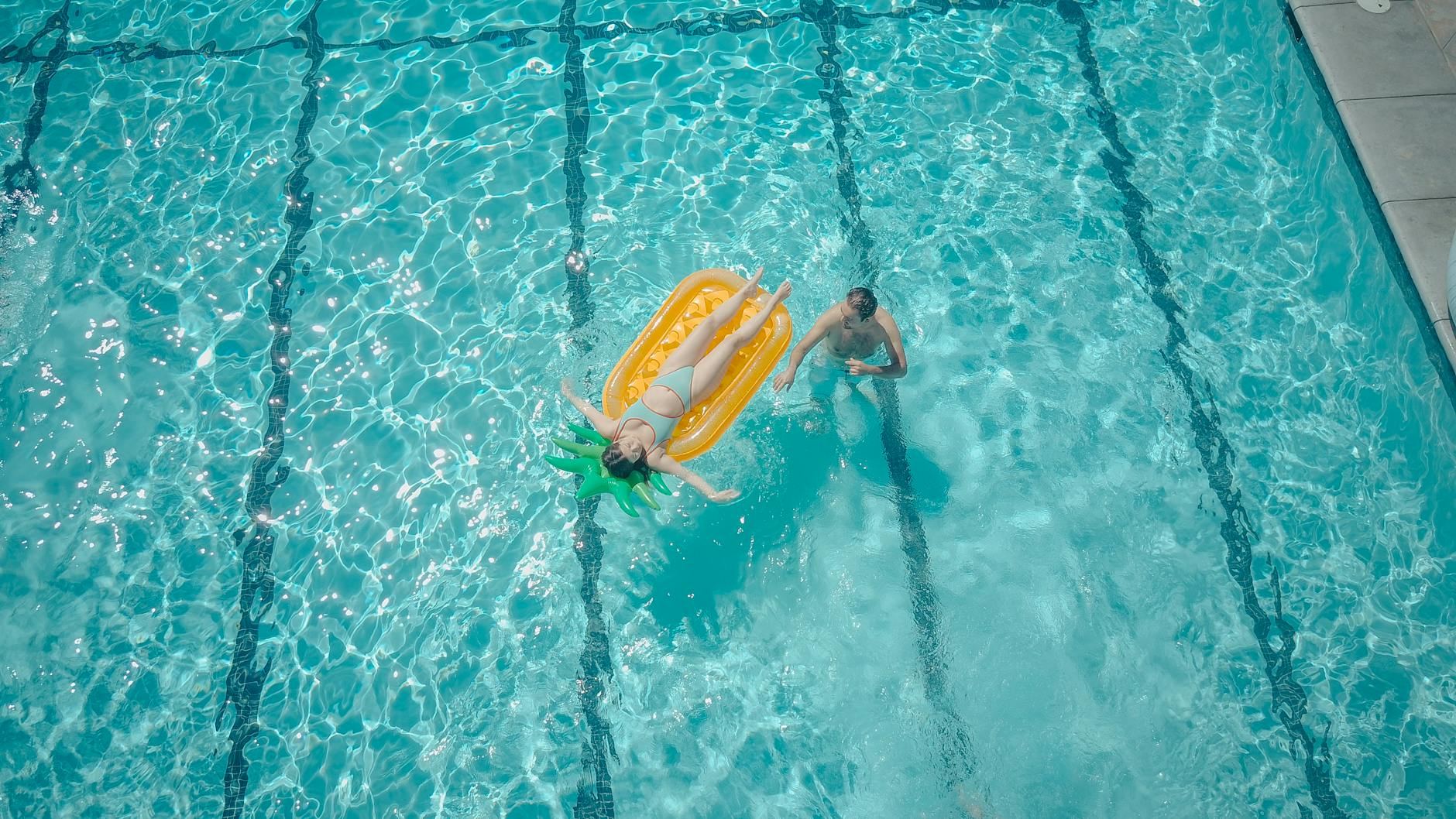 Two people enjoying a sunny day at the pool with a float. Perfect for vacation and summer themes.