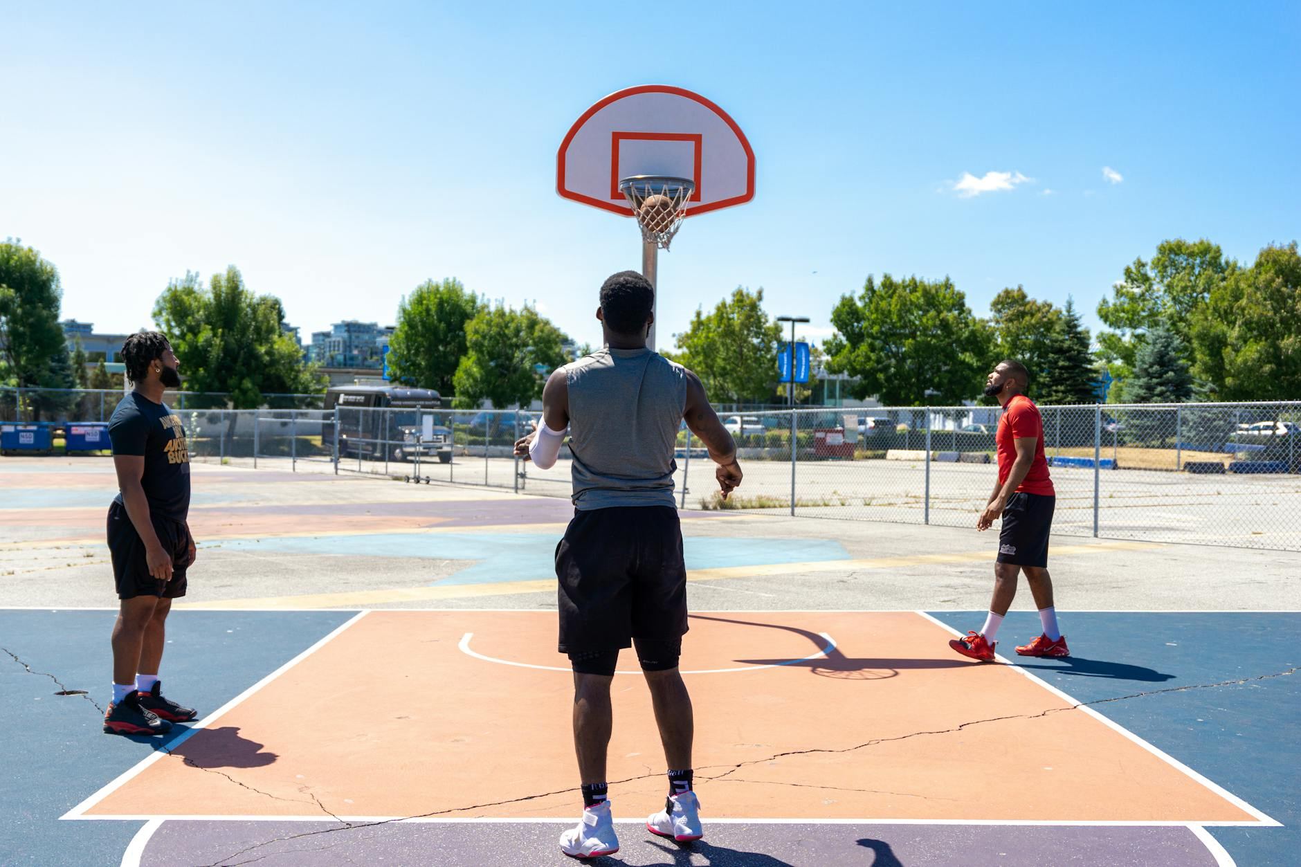 Three men playing basketball on an outdoor court on a sunny day.