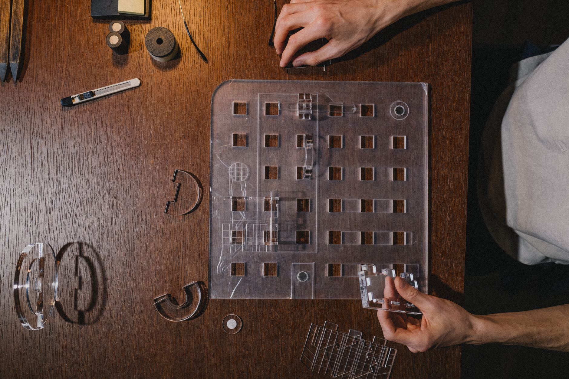 Hands assembling an architectural model with tools on a wooden table, showcasing precision and creativity.