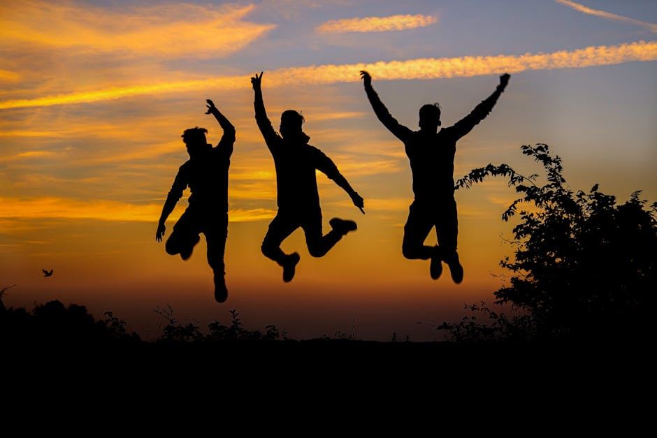 Three silhouetted figures leaping against a vibrant sunset sky with clouds.