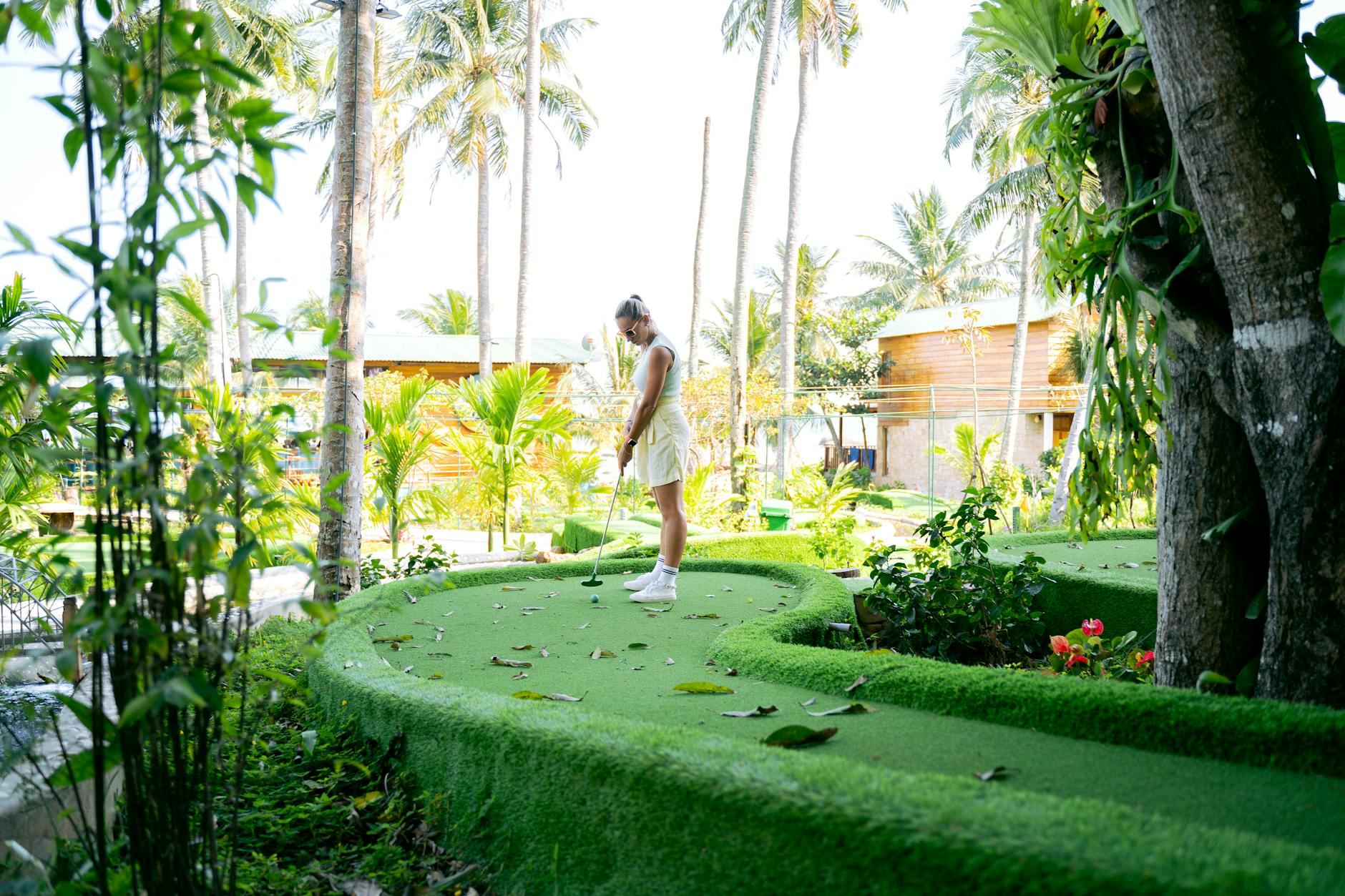 A woman enjoying a game of mini golf in a lush tropical garden with palm trees.