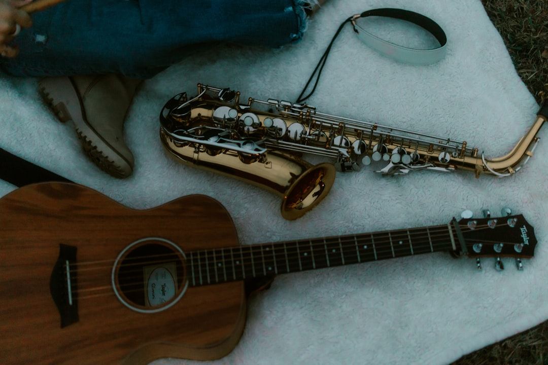 A wood acoustic guitar and a brass saxophone on a white blanket.