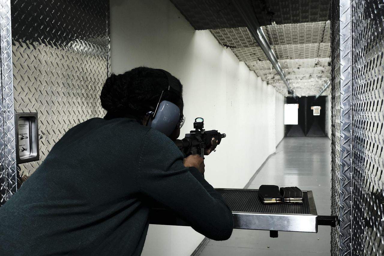 A focused woman in shooting gear aims her pistol at a target, showcasing her concentration and skill in pistol shooting.