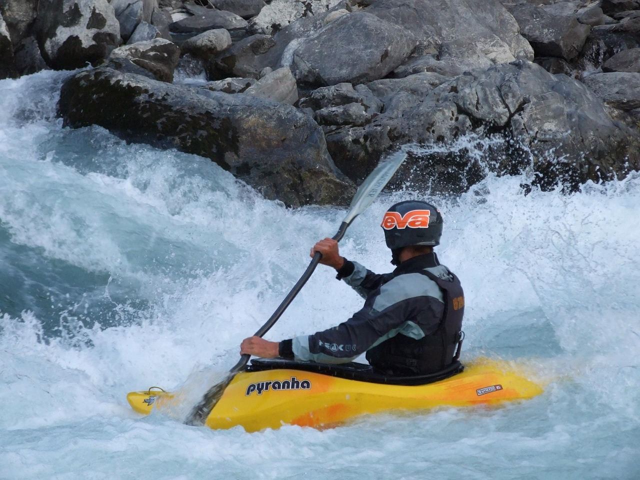 A kayaker expertly navigates through a turbulent river rapid, splashing water and showcasing thrilling adventure.