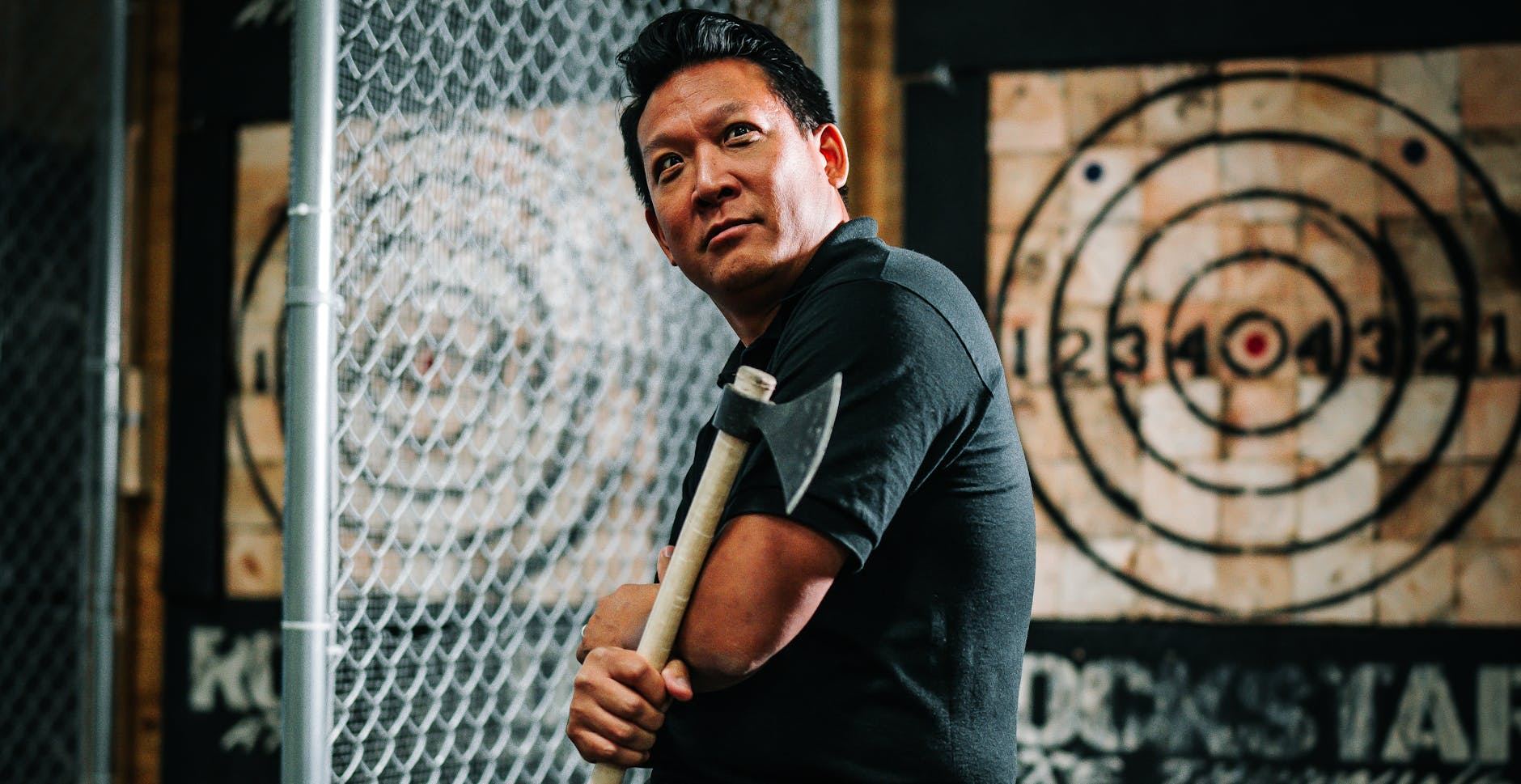 Man posing with an axe in an indoor axe throwing facility, ready for sport.
