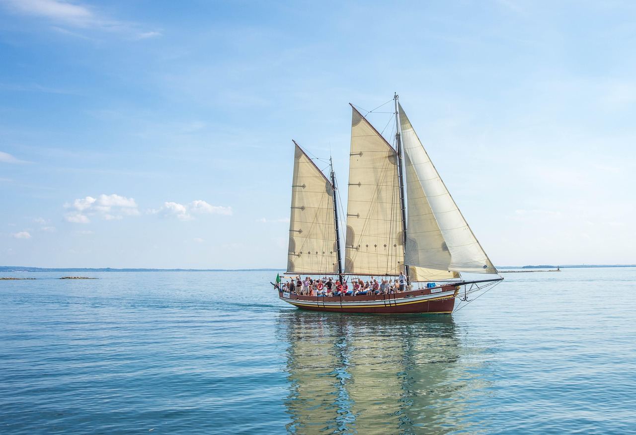 A majestic sailboat glides across the sparkling blue waters, its white sails billowing in the wind under a clear sky.