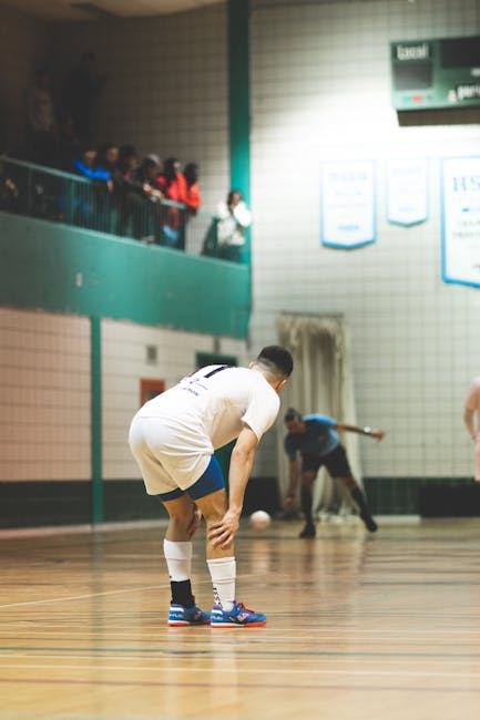 A futsal player prepares to receive the ball in an indoor gym setting.