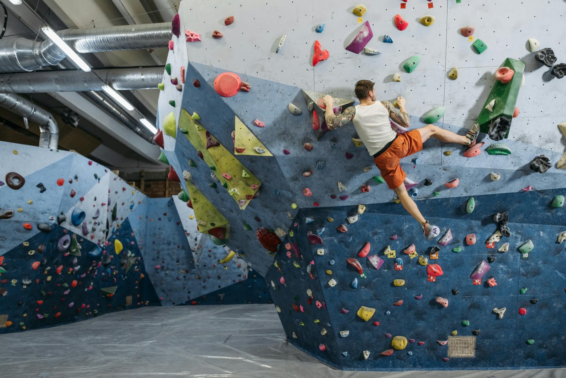 A man skillfully climbs a vibrant, textured bouldering wall, demonstrating his athletic prowess amidst bright holds.