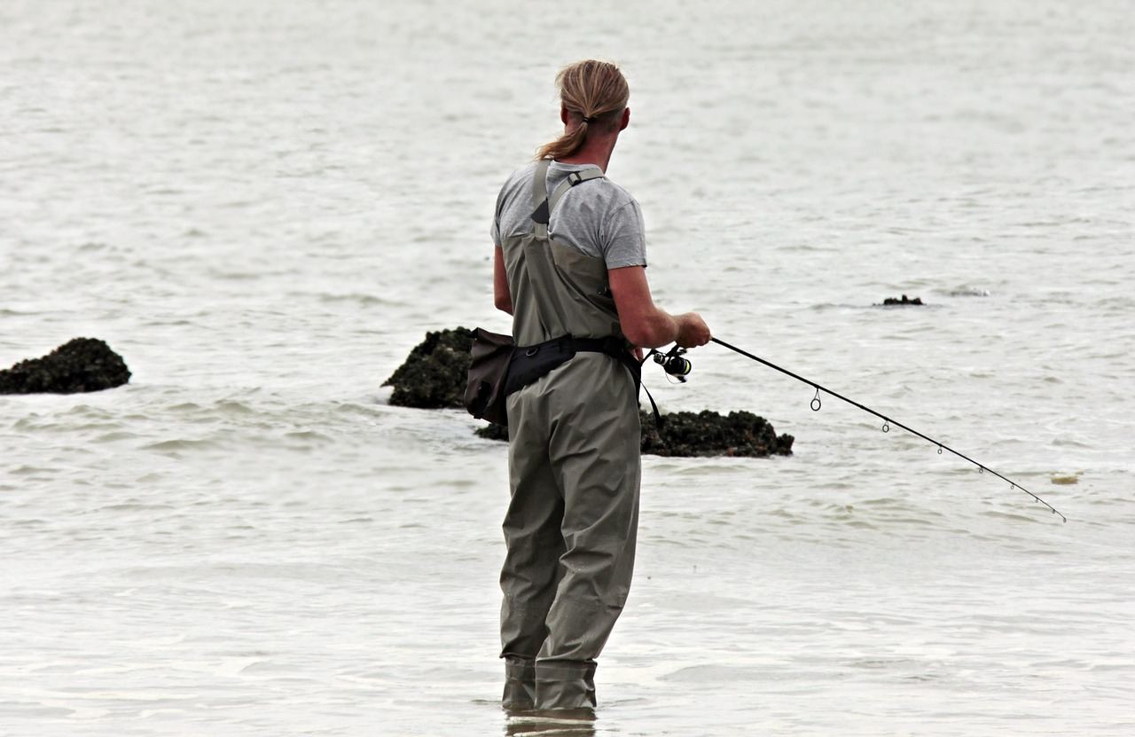 An angler stands in shallow water, fishing with a rod, exploring if pier fishing is for them.
