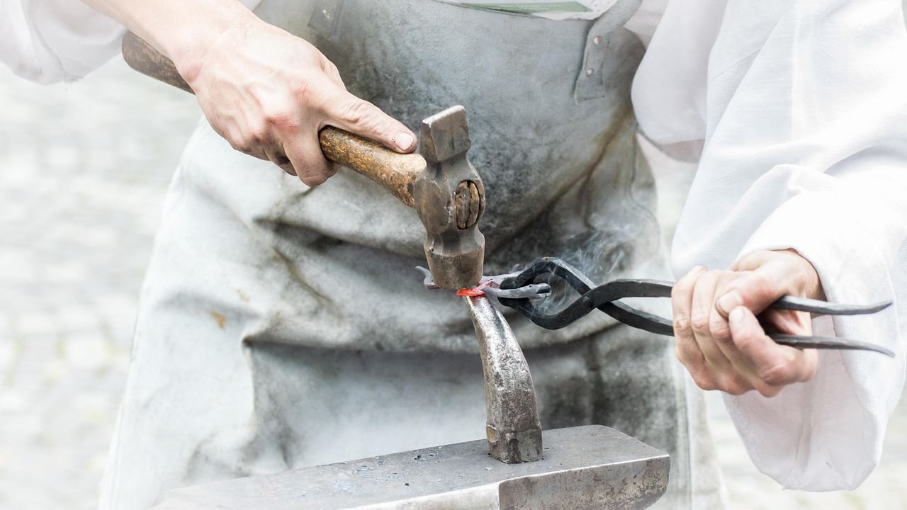 A skilled blacksmith hammers glowing metal on an anvil, sparks flying in a dimly lit workshop filled with tools.