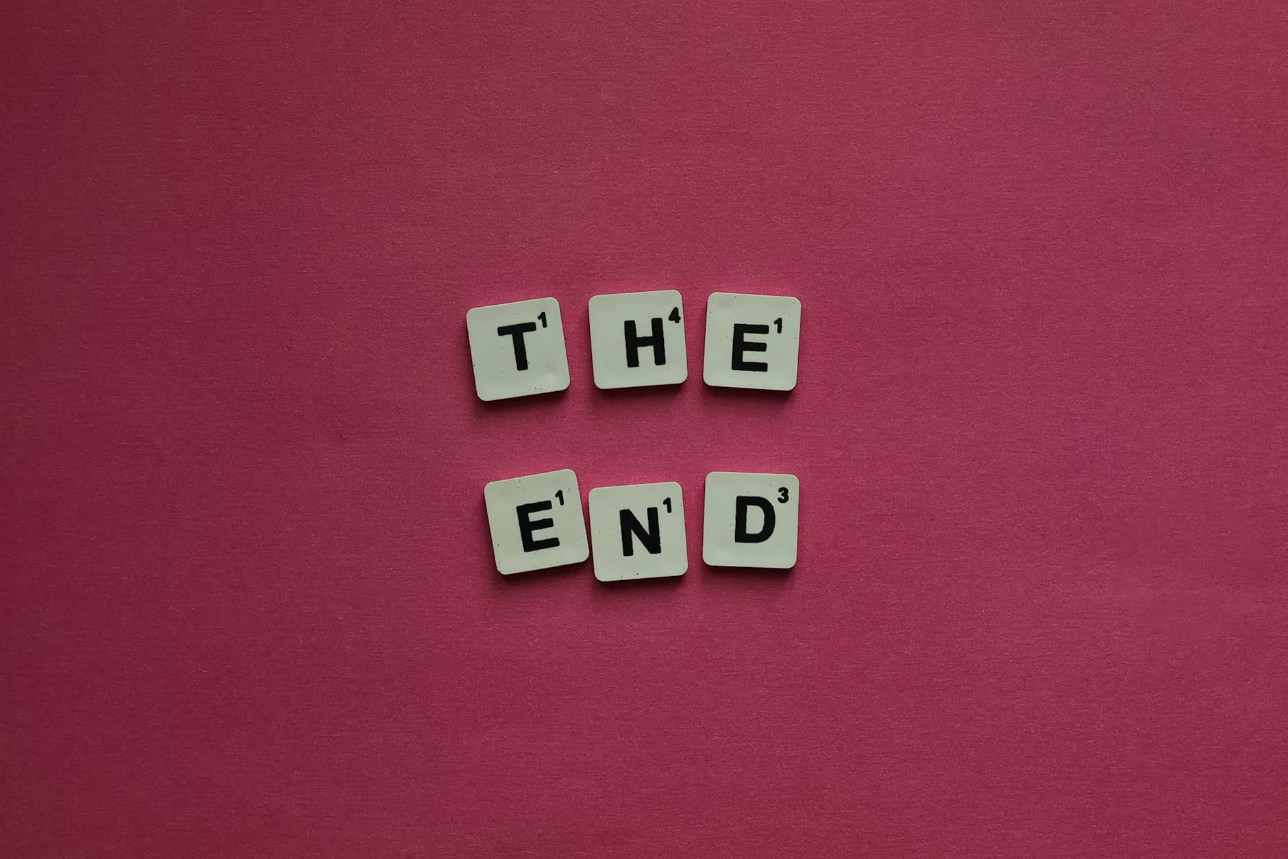 Scrabble tiles arranged to spell 'The End' contrast vividly against a bright pink background, representing the finality of a game.