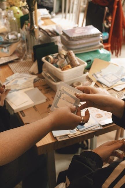 Two people exchanging scrapbook materials at a table filled with crafting supplies.